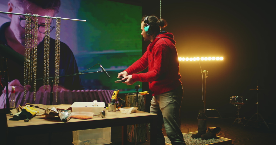 Zoom in view of male sound designer in headphones recording scratching noise against screen with video of potter creating earthenware in workshop