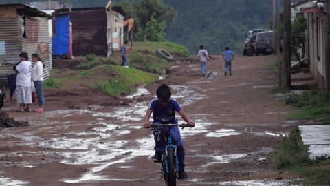 Guatemala City, Guatemala - CIRCA JUNE 2014 - Young Latino boy riding a bicycle towards the camera on a muddy road in a poor neighborhood