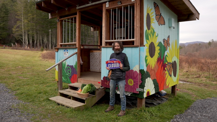 Wide shot of a hipster farmer with a big beard holding an open sign in front of his farm business in slow motion