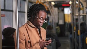 Young african american man use smartphone sitting in tram traffic typing at sunny day handsome passangers stylish transportation using way internet online texting portrait guy slow motion.