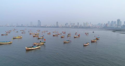 Flying sideways with Koliwada Fishermen's boats parked in foreground while the Mumbai City view in the back under a smog like hazy weather.
