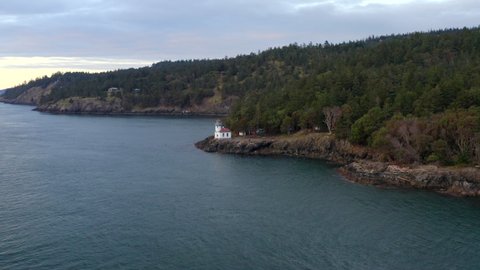 Lighthouse drone. Drone flying around lighthouse (wide shot) at sunset in the Pacific North West San Juan Islands. Birds flying over ocean with forest in background. Lighthouse 4k
