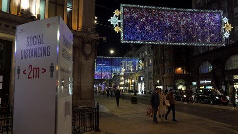 London , United Kingdom (UK) - 11 07 2020: People walk past a social distancing sign and the Oxford Street Christmas lights