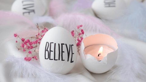 Footage of igniting a candle in Easter eggs Composition. Words drawn with pen. Believe. Cozy home interior decor, burning candles hygge, decoration and easter concept - candles burning