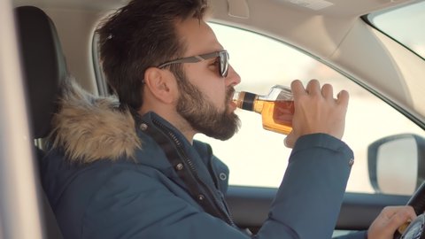 Drunk Driving Sitting On Car.Tired Man Illegal Vehicle Driving.Drunken Drive Risk Car Accident.Man Holding Alcohol Bottle In Car. Dangerous On Road Drunk Driving.Stress Unlawful Intoxicated Drive Auto