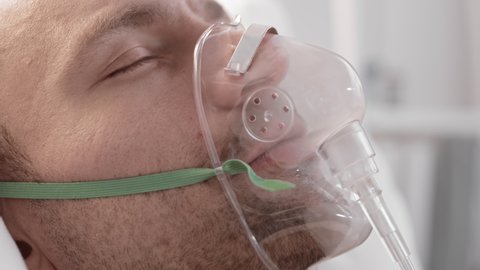 Extreme close-up of young Caucasian man with eyes closed, breathing with help of oxygen mask on his face