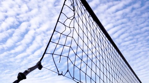 Torn volleyball net against the backdrop of bright cirrus clouds. Silhouettes of a stretched net with a knotted rope on an abandoned sports ground