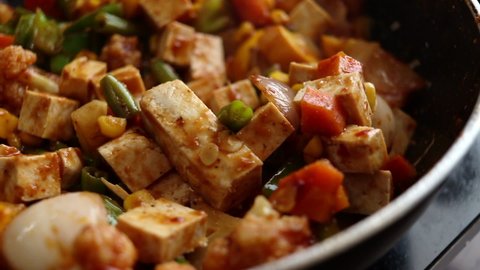 Close up of freshly cooked homemade vegan tofu with healthy vegetables in a spicy chilli sauce. Steaming hot saucy Chinese food.