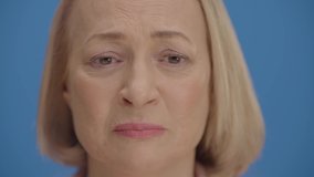 Old woman’s face is sad in front of the Blue Background. Concept of being sad. Slow motion video.
