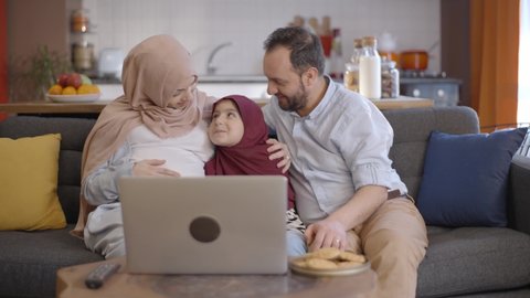 The Muslim woman wearing a hijab is happy when her daughter and husband video chat with their family and show her belly for the baby to be born. New sibling concept.