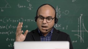 Indian young teacher man sitting wearing headset teaching online video conference live stream by laptop. Asian teacher teaching mathematics class webinar online for students learning.