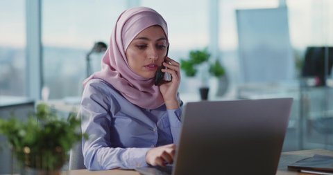Arabic young formal businesswoman talking business talk in corporate office working in call center using laptop computer.