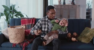 African american young daddy playing with little baby son in living room relaxing together on couch. Families. Affectionate moments. Childhood.
