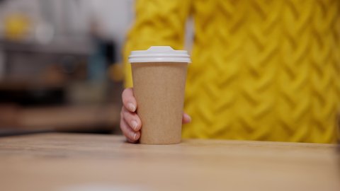 Young female Caucasian hand pushing disposable coffee cup to camera. Unrecognizable barista serving hot drink in cafeteria or cafe. Food service occupation.