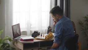 A young cute man plays chess with a different video of a house during a pandemic