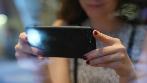 Smartphone in landscape orientation, held by woman. Blurred face of user on background, shoot through window, street reflection on the glass. Lady watch movie or read from mobile device