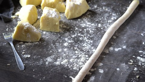 Hand cutting gnocchi with a scraper. Creating fresh Italian pasta on dark table with flour. homemade gnocchi preparation steps: gluten free mashed potato puree roll