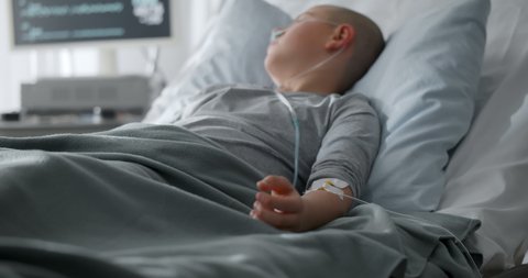 Teen boy lying in hospital bed receiving medication through intravenous dripper. Sick child patient with cancer resting in bed during chemotherapy treatment