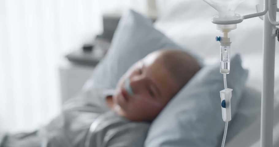 Focus on intravenous drip with sick kid lying in hospital bed on background. Teen boy patient with cancer resting in bed having medication in dropper Royalty-Free Stock Footage #1067978267