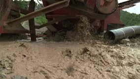 Video from a low angle, focusing on downward area of stone pit machine, as it spreads water on the work site, green trees can be seen in background.