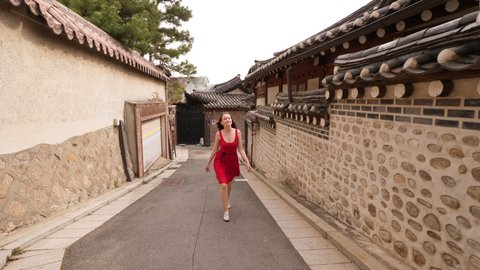 Curious woman watch around, walk at small alley of Bukchon Hanok Village. European tourist stroll at Korean traditional village. Stone walls, restored old low-rise houses with tiled roofs