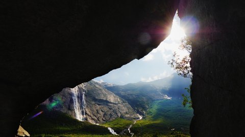 The sun shines through the arch in the rock, where you can see the picturesque valley surrounded by high mountains. The amazing nature of Norway, the tourist's dream