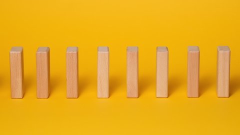 Domino effect, row of wooden domino falling down with yellow background.