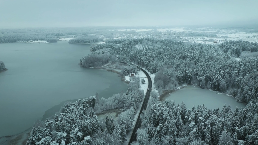 Aerial view of vehicle driving on winter road between two lakes in Lithuania.