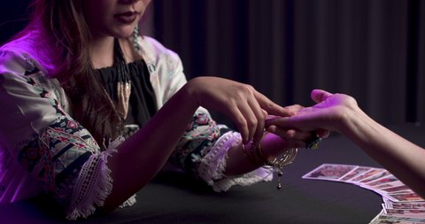 The person extends a hand to young asian woman fortuneteller. Gypsy girl points the palm to make future prediction. Astrology, occultism and paranormal concept.