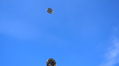 British currency pound coins spinning and falling from blue sky in slow motion; low angle view, copy space.