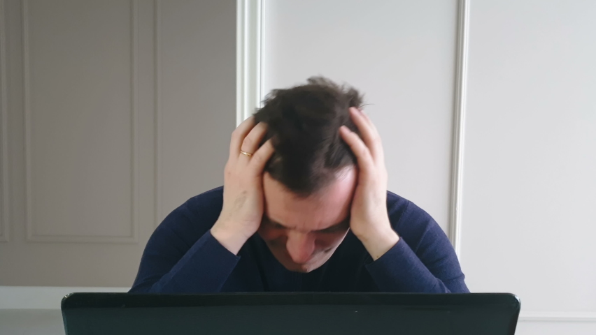 unhappy young caucasian worker looks at laptop screen, shocked by  broken gadget or operational problems. frustrated person cries over overdue debts and worries about stock market price drops Royalty-Free Stock Footage #1068004064