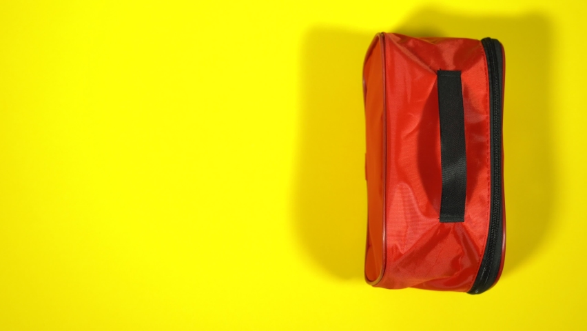 Closeup top view flatlay 4k stock video footage of male hand taking red case of first aid medical kit isolated on bright yellow background  | Shutterstock HD Video #1068006650