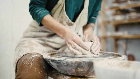 Pottery workshop. Close up of female artist hands working with clay on pottery wheel, tracking shot, slow motion.