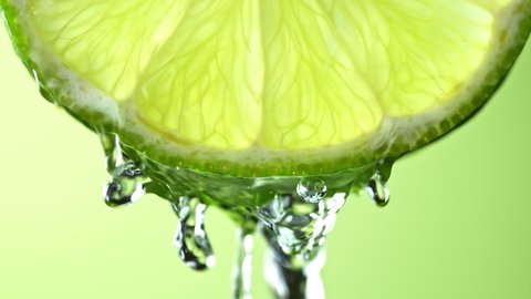 Super Slow Motion Macro Shot of Flowing Water from Lime Slice on Green Background at 1000fps.