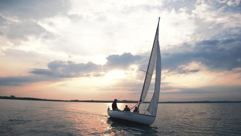 Men sailing a beautiful white yacht boat across the river. Cinematic red sunset. Scenery on lake. Water activities. Summertime.