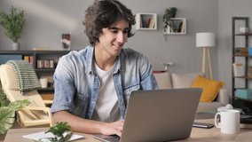 smiling young man sits at his desk typing at the laptop looking satisfied at the computer screen,positive arab male freelancer working from home office using notebook writing email - Powered by Shutterstock - Get 15% off with code: PIKWIZARD15
