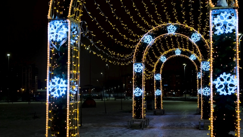 Arches decorated with garlands in city park. Concept. People pass through arches with garlands. People walk under arches decorated with garlands glowing brightly in evening