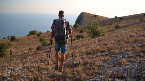 travel mountain hike following shot of man travel on crimea black sea, hiking mountain hike travel. Spbd rear view of tourist with backpack walk with trekking poles. male, summer, gear concept