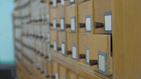 A male hand searching cards in old wooden card catalogue. A vintage library catalogue, for a convenient and quick search for a book. Search for information in the card file in the library. 4k footage