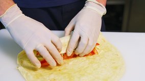 Cooking meat and cheese pita with vegetables. Hands in latex gloves roll up a pita roll. Concept video.