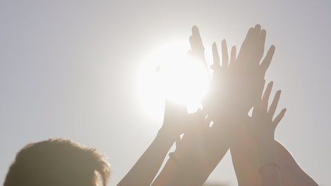 Close up, people raise their hands up to the sky and join their palms together in the bright summer sun. Strengthening team spirit by joining hands together. 