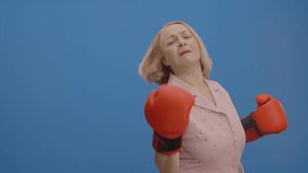 The old woman who makes a boxing by himself with box gloves in front of a blue background. Boxing concept on blue background. - Powered by Shutterstock - Get 15% off with code: PIKWIZARD15