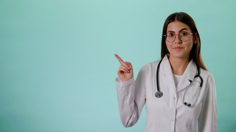Caucasian Smiling Female Doctor Wear White Uniform And Stethoscope Pointing On Copyspace Isolated Over Blue Background In Studio, Place For Text Or Image, Showing Empty Space For Mock Up