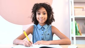 Webcam view of a pretty curly African schoolgirl wearing a headphones, a pretty biracial girl fill exercises book in with a pen watching online video classes. E-learning concept