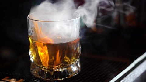 glass of whiskey with ice and smoke on bar