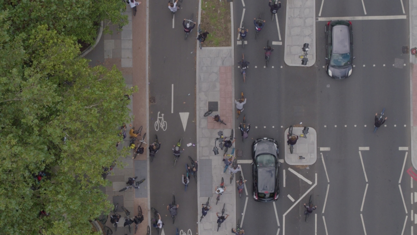 Aerial drone top down view tracking forward flying over a busy main road in London with lots of cyclists riding down the road with some cars and London buses
