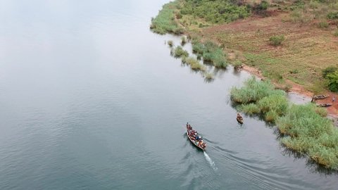 Big wooden boat powered by an outboard motor full of people travelling slowly on the water of Lake Tanganyika Zambia Aerial Video