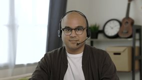 A man around the age of 35 wearing headset. Working at home by meeting video conference looking at camera. Asian businessman work from home talking on screen.