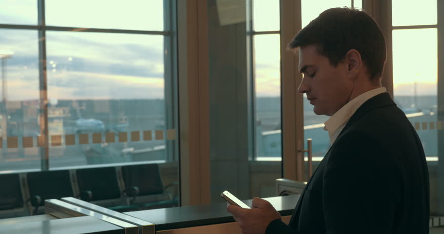 Young serious businessman typing text message on smart phone and looking out the window at airport | Shutterstock HD Video #10680578