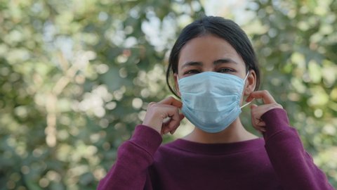 close view shot of a beautiful young Asian Indian female removing a protective mask off the face and smiles looking at the camera in a broad daylight amid covid 19 pandemics. Post-vaccination concept